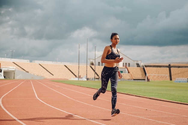 Sporty female runner running on stadium track