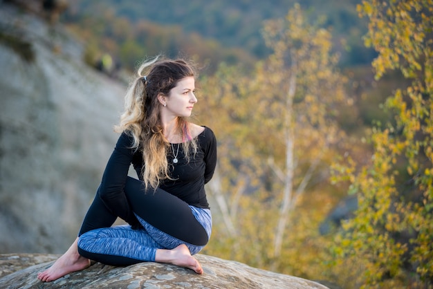 Photo sporty fit woman is practicing yoga on the top of the mountain