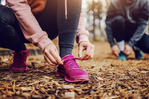 Sporty fit young woman tying shoelace while crouching on trail in nature and getting ready for running.