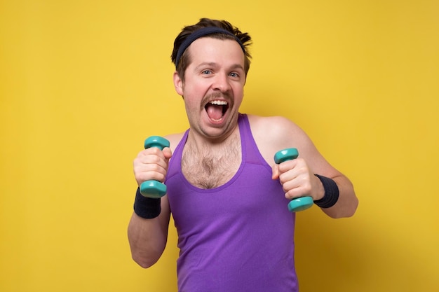 Sporty fitness man doing exercise with dumbbells isolated on yellow background