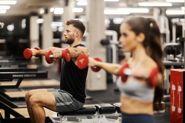 Sporty friends doing lateral raise in a gym and sitting on a bench