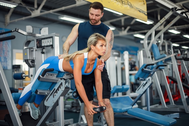 La ragazza sportiva che fa il peso si esercita con l'assistenza del suo istruttore personale alla palestra.