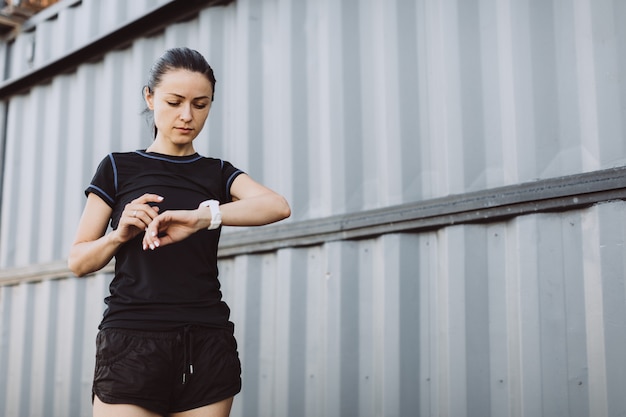 Sporty girl dressed in black checks her heart rate on a smart watch.