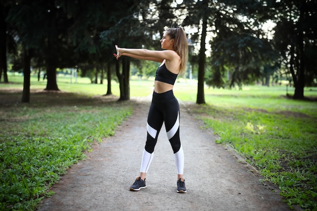 스포츠 여자 는 공원 에서 몸 을 따뜻 하게 하기 위해 운동 을 하고 있다