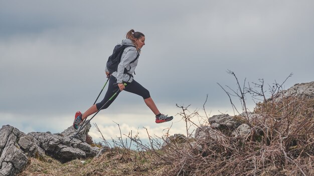 Sporty girl jumps between the stones during an alpine trekking