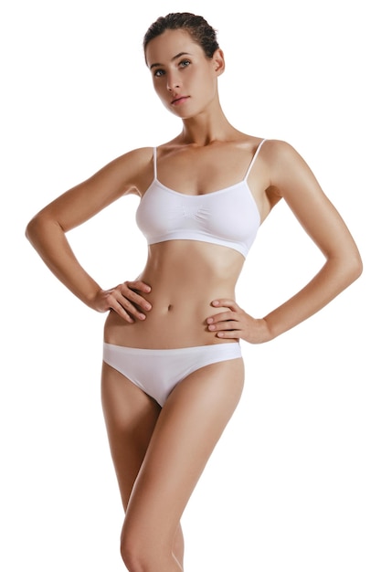 Sporty girl in white underwear with bundled hair hands on hips posing in studio isolated on white background Plastic surgery Augmentation or reduce of a breast cellulite removal Closeup