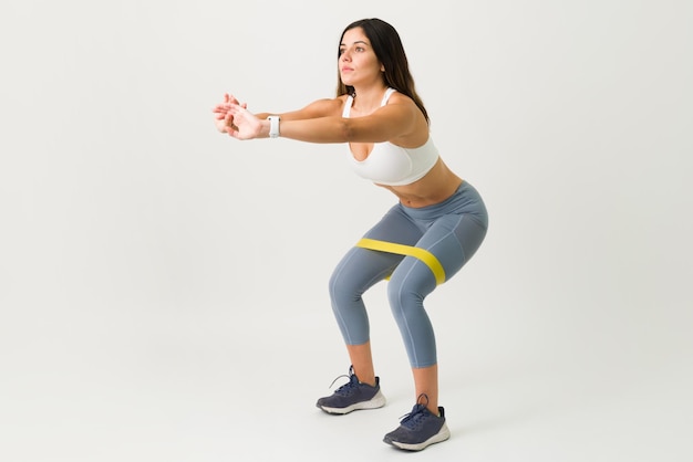 Sporty gorgeous woman in activewear doing squats with a strength band. Active young woman with toned abs squatting with an elastic band on her legs