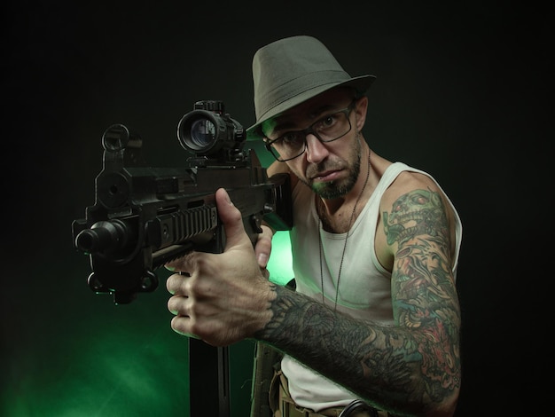 The sporty guy with a tattoo poses with an automatic rifle