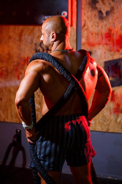 Photo sporty handsome strong man posing with sports rope on the background of the gym. a strong bodybuilder with perfect abs, shoulders, biceps, triceps and chest.