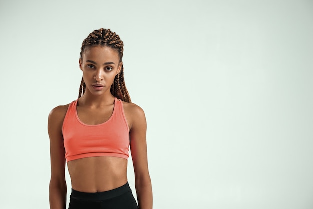 Sporty and healthy young african woman in sportswear standing against grey background and looking at