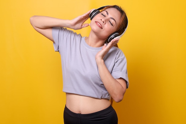 Sporty jonge vrouw luistert naar muziek met koptelefoon op gele achtergrond
