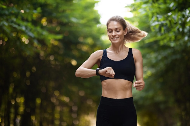 Спортивная дама смотрит на фитнес-браслет во время бега на свежем воздухе