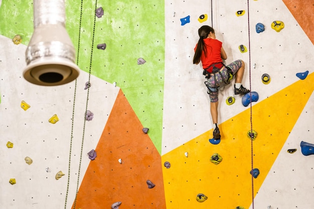 Спортивная маленькая девочка, восхождение на искусственный валун на практической стене в тренажерном зале