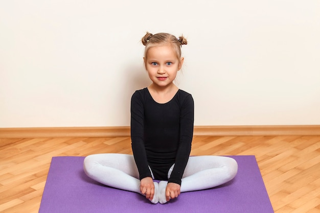 Foto bambina sportiva che si siede nella posizione del loto sul tappeto viola