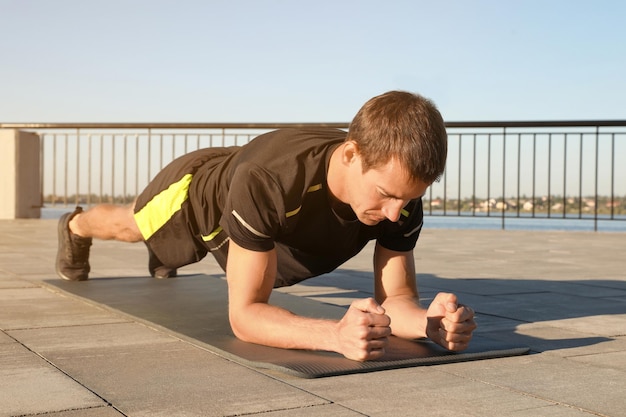 Спортивный мужчина делает упражнения на доске на коврике на открытом воздухе