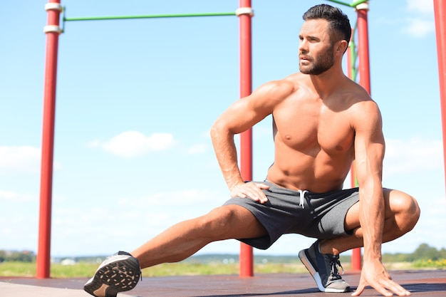 Sporty man doing workout stretching exercises for legs outdoors.