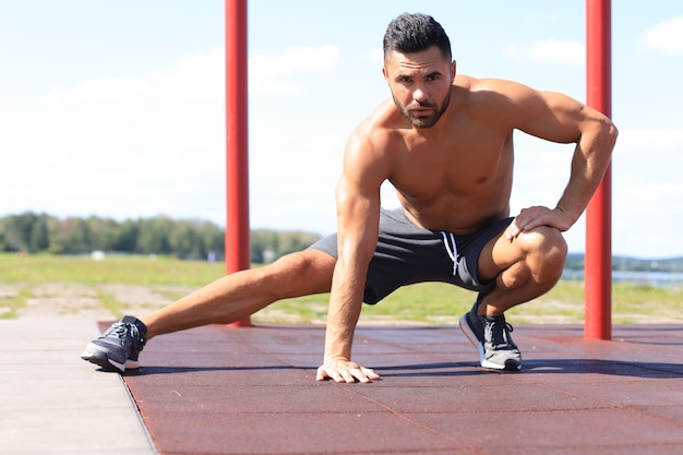 Sporty man doing workout stretching exercises for legs outdoors.