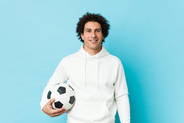 Sporty man holding a soccer ball happy, smiling and cheerful.