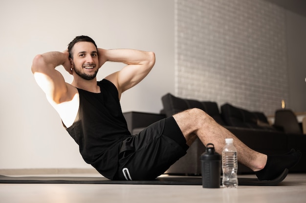 Sporty man pumping press lying on mat. Fit happy man doing fitness exercises on floor at home. Black sport clothes. Muscular man doing his favorite morning exercise.