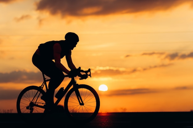 Sporty man in silhouette riding bike on paved road