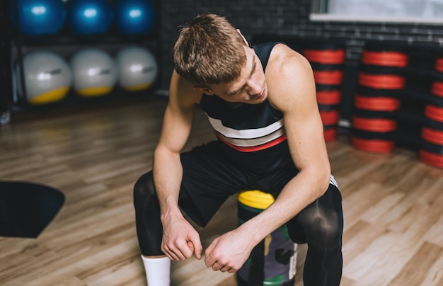 Sporty man sitting on sandbag relaxing after exercises in the gym Attractive athletic male rest after hard workout with weight training with copy space for your text or advertising