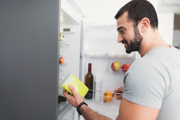 Sporty man stands in the kitchen and takes fresh vegetables