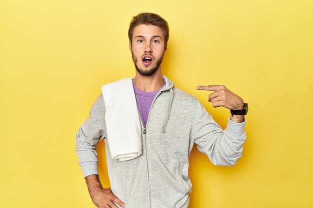 Sporty man in sweatshirt and towel on yellow pointing to the side