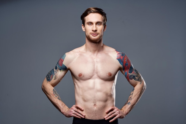 Sporty man tattoos on his arms naked torso bodybuilder gray background