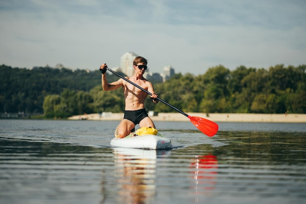 ビーチを背景に海の手漕ぎボードに美しいボディパドルを持つスポーティな男