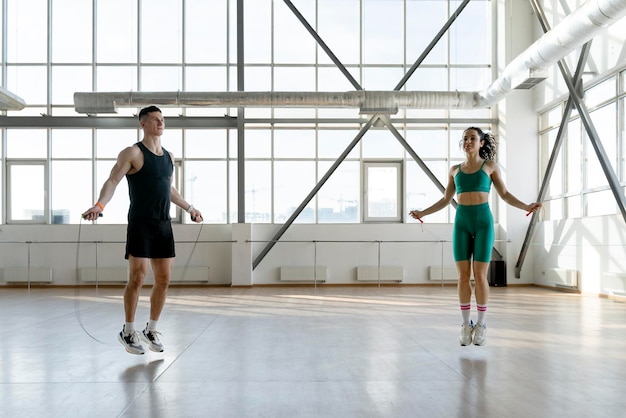 Sporty man and woman perform jumping rope in light sports hall Soncept of healthy lifestyle