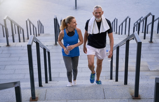 Sporty mature couple man and woman in sportswear looking pleased walking up the stairs after