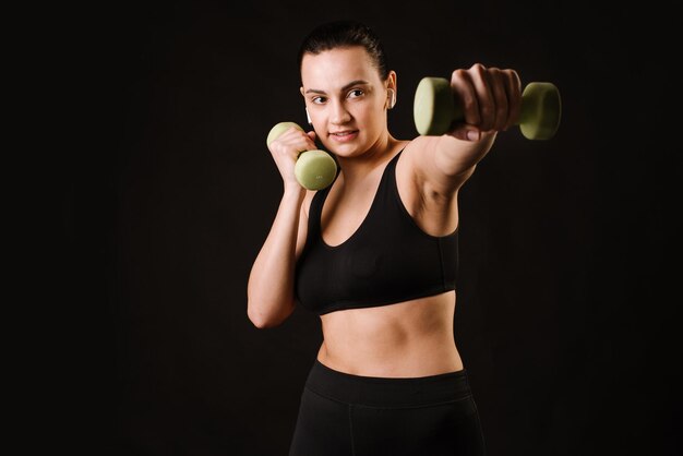 Sporty model woman doing exercises with dumbbells on black background. Copy space