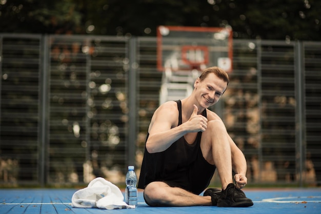 Sporty muscular man tying laces on sport sneakers before morning run at outdoor basketball court