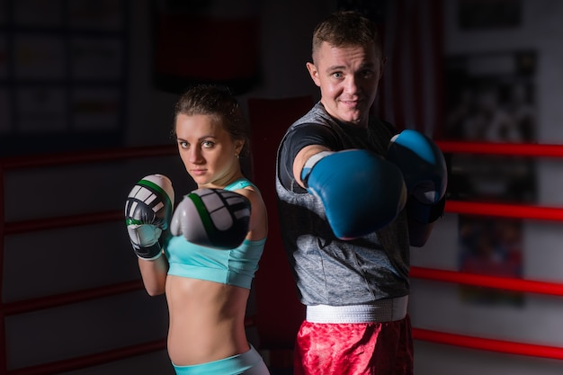 Спортивная пара в спортивной одежде и в боксерских перчатках, стоящих на обычном боксерском ринге в тренажерном зале