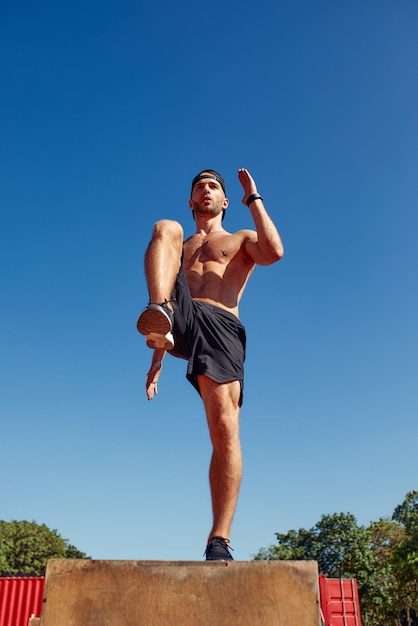 Sporty physically fit man doing stepup exercise on wooden box while doing gym training in sports club