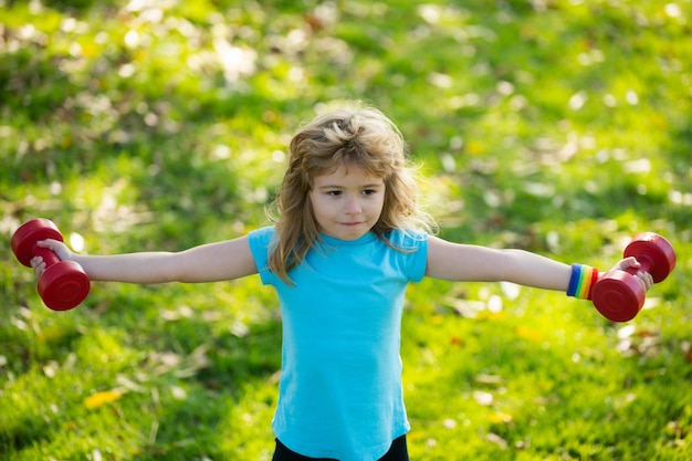 公園のジムのトレーニングの子供スポーツマンの子供の頃のactiのダンベルが付いているスポーティーな肖像画の子供のフィットネスの子供