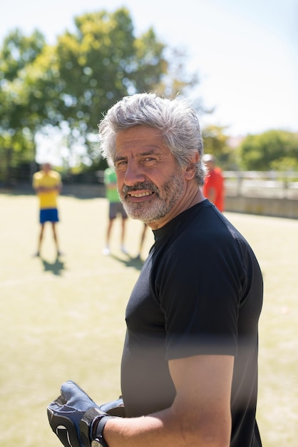 Sporty senior goalkeeper ready for match. Man with grey hair and beard in gloves smiling at camera. Football, sport, leisure concept