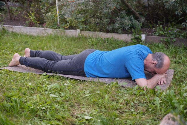 Sporty senior man resting after yoga fitness pilates practice lying on mat on grass