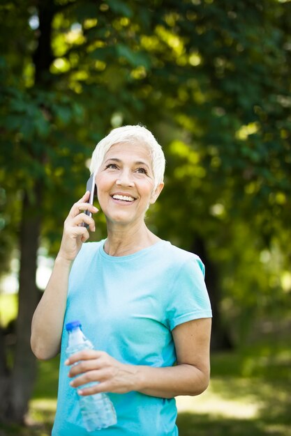 Sporty senior woman using mobile phone in the park