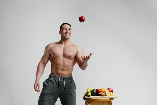 Sporty sexy guy posing on a white background with bright fruits. Diet. Healthy diet