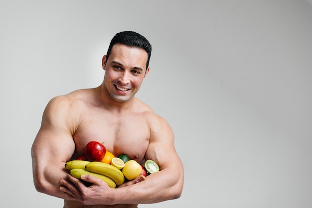 Sporty sexy guy posing on a white background with bright fruits. Diet. Healthy diet