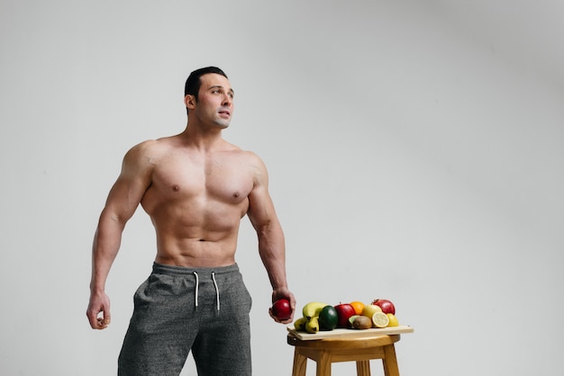 Sporty sexy guy posing on a white background with bright fruits. Diet. Healthy diet.