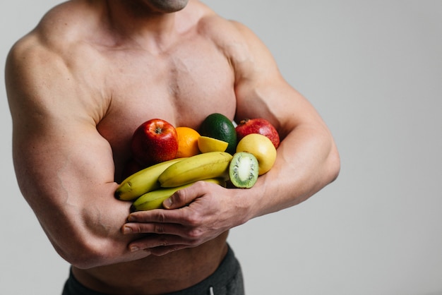 Sporty sexy guy posing on a white space with bright fruits. Diet. Healthy diet.