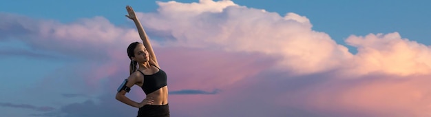 A sporty slim girl in leggings and a top is standing near a concrete wall with a training mat resting between exercises