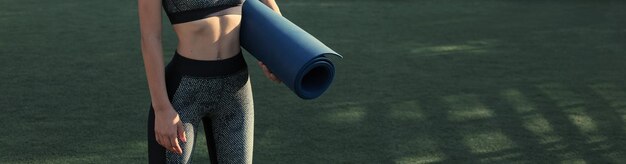 A sporty slim girl in leggings and a top is standing with a training mat resting between exercises