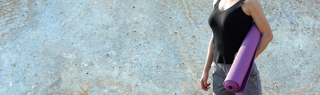 A sporty slim girl in leggings and a top is standing with a training mat resting between exercises