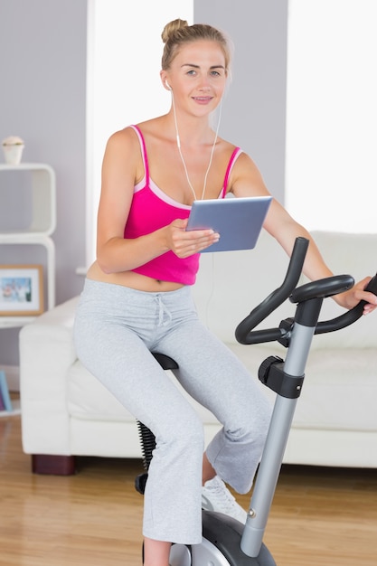 Sporty smiling blonde training on exercise bike using tablet