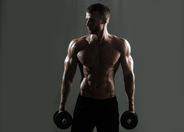 덤벨을 가진 스포츠 몸통의 남자 근육이 많은 남자 스튜디오에서 운동을 하고 강한 남성 벌거벗은 남자