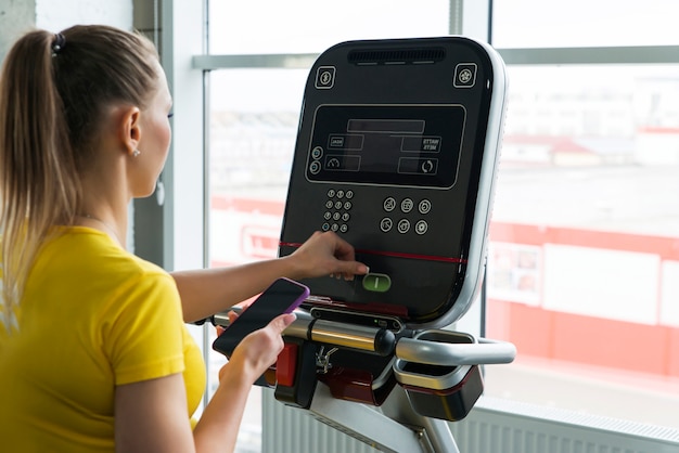 Sporty woman adjust settings on treadmill machine in gym