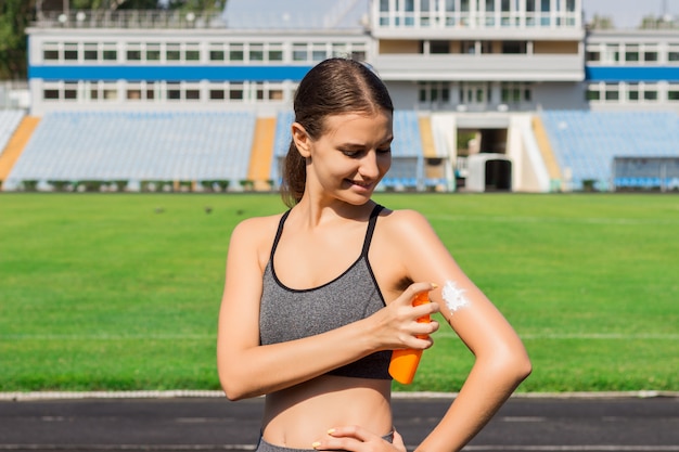 Sporty woman applying sunscreen on stadium before run. Sports and healthy concept